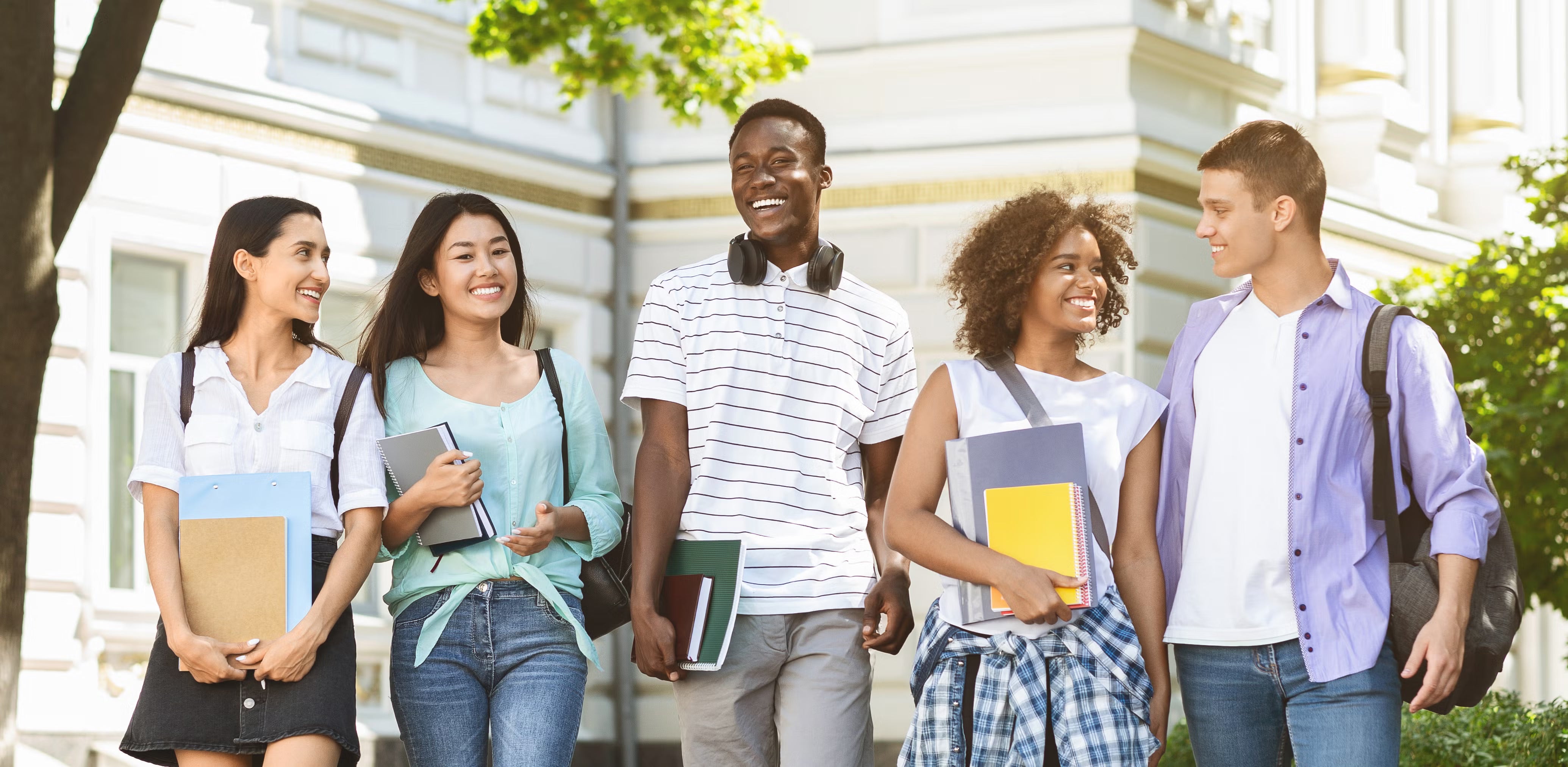 Happy students walking outside a class building, holding books and laughing