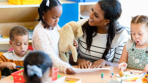 The mid adult female teacher manages the classroom full of busy young children.