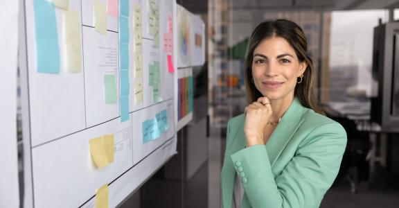 business woman looking at the camera in front of a complex project board