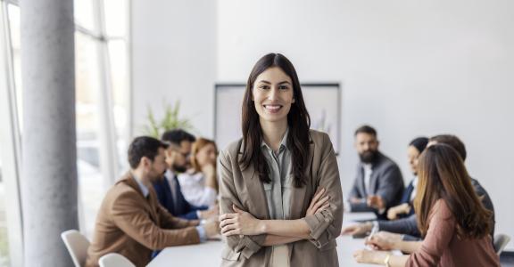 Young woman facing the camera with a group of coworkers meeting behind her