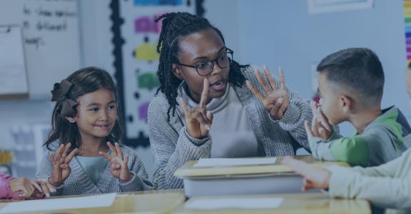 A black elementary teacher sitting at desks having a math lesson with two small children.