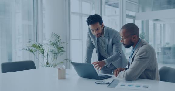 two men working together in a business office with a laptop and some papers