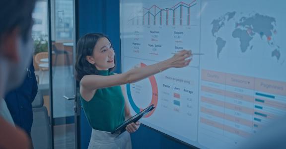 woman in a boardroom pointing out marketing analytics on a big screen