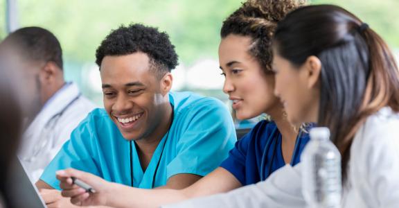 Diverse male and female nursing students review information on a laptop for a test.