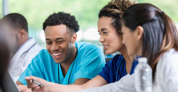 Diverse male and female nursing students review information on a laptop for a test.