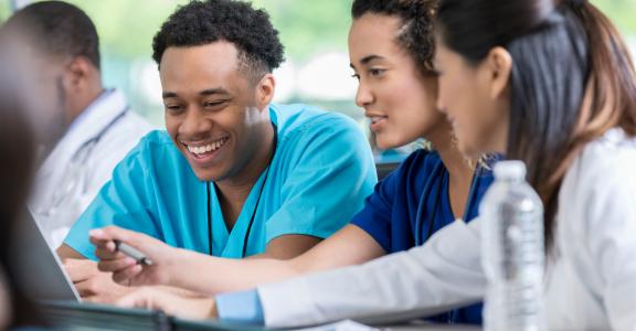 Diverse male and female nursing students review information on a laptop for a test.