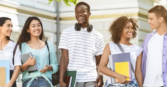 Happy students walking outside, holding books and laughing