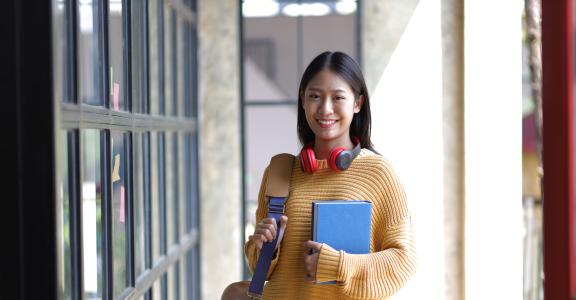 Portrait of a female student outside a classroom holding a bag and a book