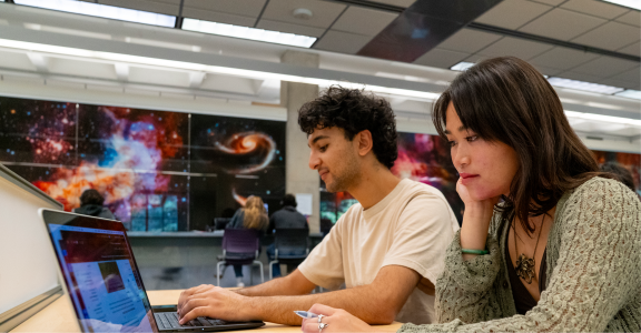 Two students studying in library with galaxy pictures behind them