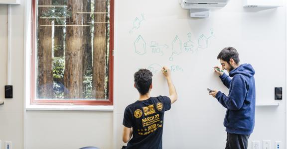 two students writing chemical structures on whiteboard