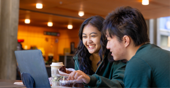 two students smiling looking at their laptop