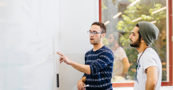 Two students discussing in front of a whiteboard