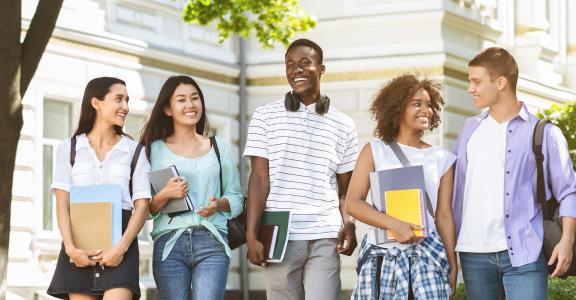 Happy students walking outside a university, holding books and laughing