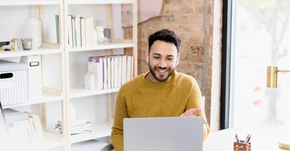 The young adult man uses his laptop to video conference with friends.