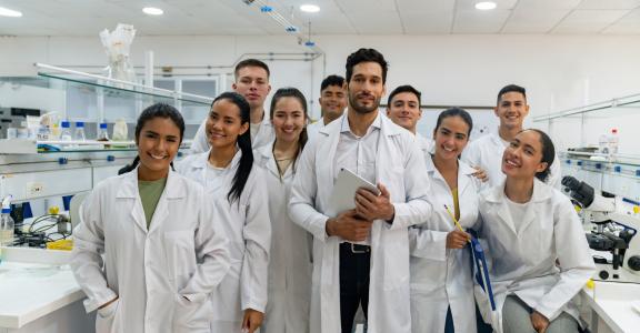 Portrait of a happy Latin American science teacher with a group of students in the laboratory and looking at the camera smiling