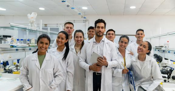Portrait of a happy Latin American science teacher with a group of students in the laboratory and looking at the camera smiling