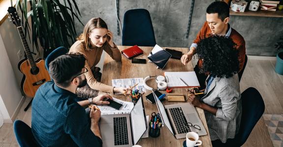 High angle view of multi-ethnic group of coworkers collaborating on a project with their laptops and data sheets