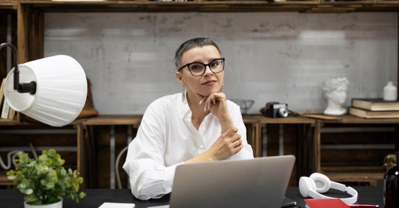 Business woman with a short haircut sits at her desk in glasses and looks at the camera.