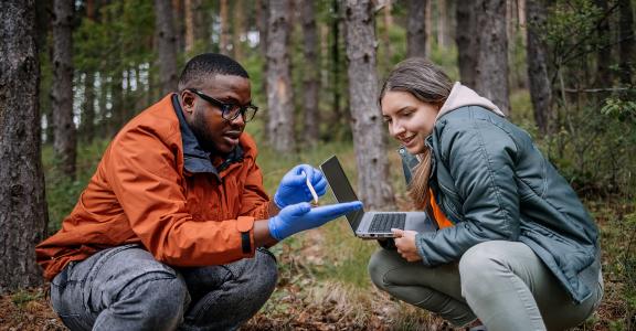 biologist explaining project to a science writer outdoors in a forest.