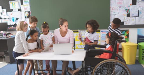 Students using digital tablet while teacher interacting with students in classroom at school
