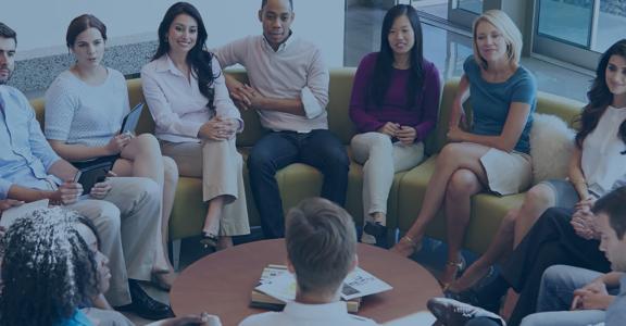 Group of professionals sitting in a semi-circle while a presenter talks