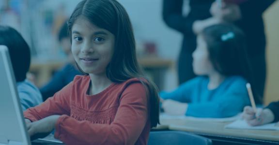 Young girl smiling at camera with open laptop, other student