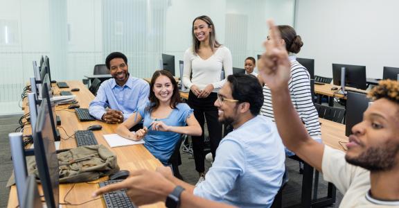 Diverse group of students actively participating in a computer lab class, showing engagement and teamwork.