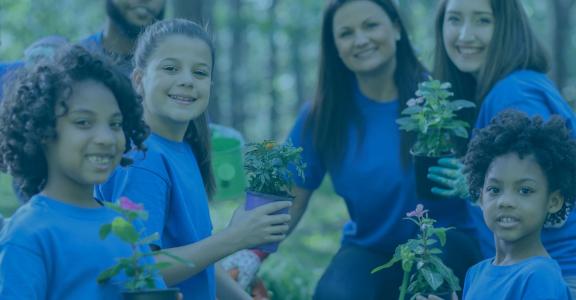 Kids with blue shirts holing plants and smiling at camera