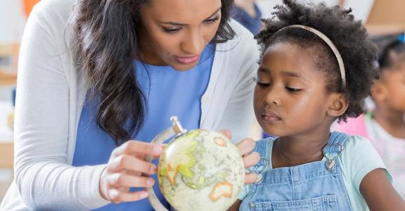 teacher showing young child a globe of the world