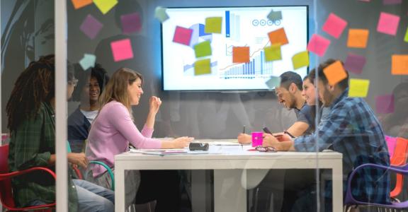 a group of people in a glass office with colorful Post-its p