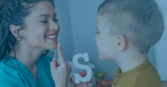 Woman smiling at young boy while point at mouth and holding 