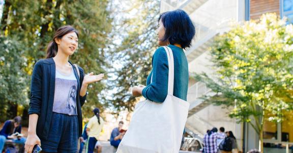 Open Campus: Two students talking in a campus plaza surround