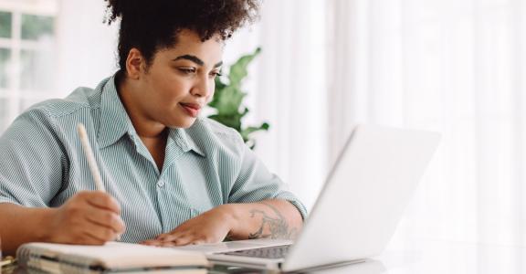 Confident woman sitting at desk using laptop and taking note
