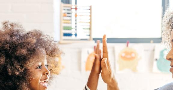 teacher high-fiving a little girl while they stack blocks to