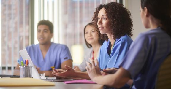 medical debrief session with 4 people in medical clothes talking about patients