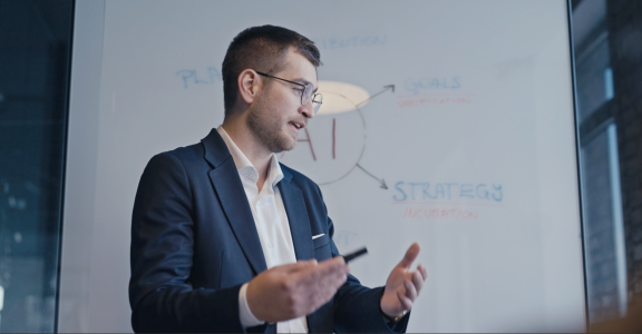 man talking in front of white board with AI strategies written on it.