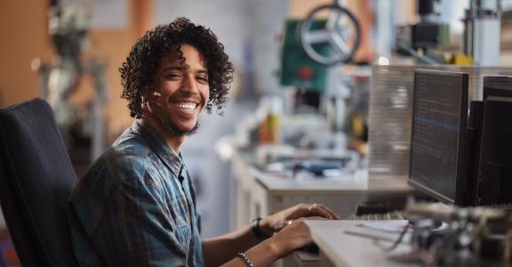 Happy African American male programmer working on desktop PC in a lab and looking at camera