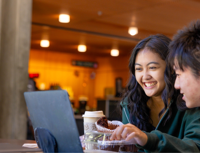 two students smiling looking at their laptop