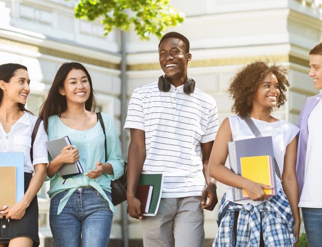 Happy students walking outside a university, holding books and laughing