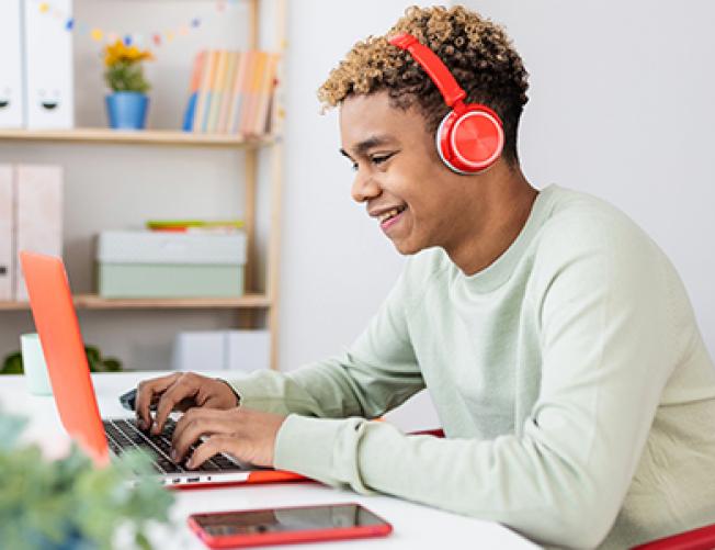 high school young man studying at a laptop with earphones on
