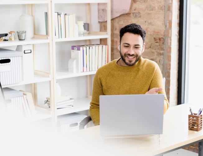 The young adult man uses his laptop to video conference with friends.
