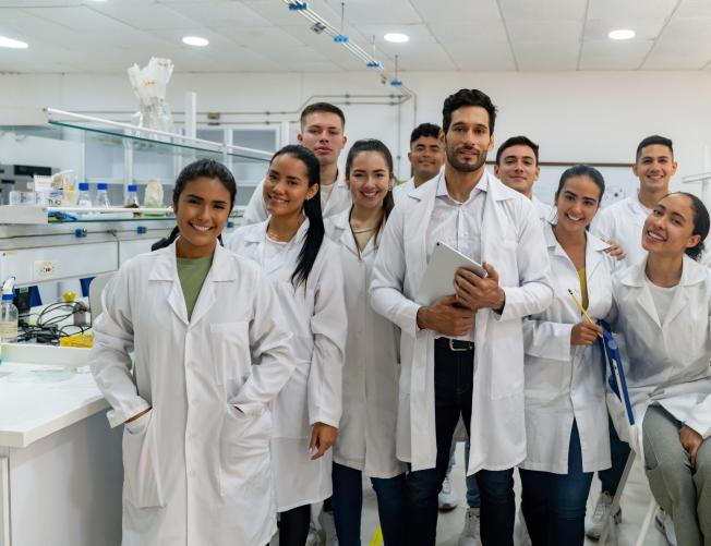 Portrait of a happy Latin American science teacher with a group of students in the laboratory and looking at the camera smiling