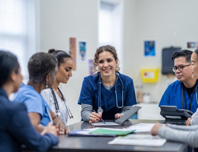 mall group of medical professionals gather around a table as they meet together to discuss patient cases