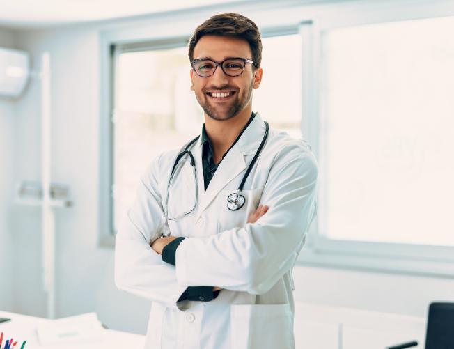Portrait of handsome male doctor with stethoscope over neck working while looking at camera in the medical consultation.
