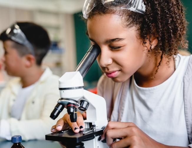 African-american schoolgirl pupil student using working with microscope at biology chemistry lesson class at school lab. 