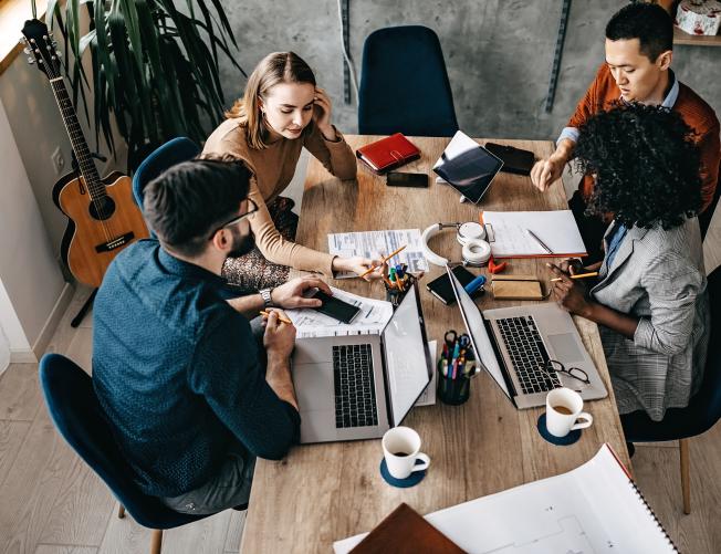 High angle view of multi-ethnic group of coworkers collaborating on a project with their laptops and data sheets