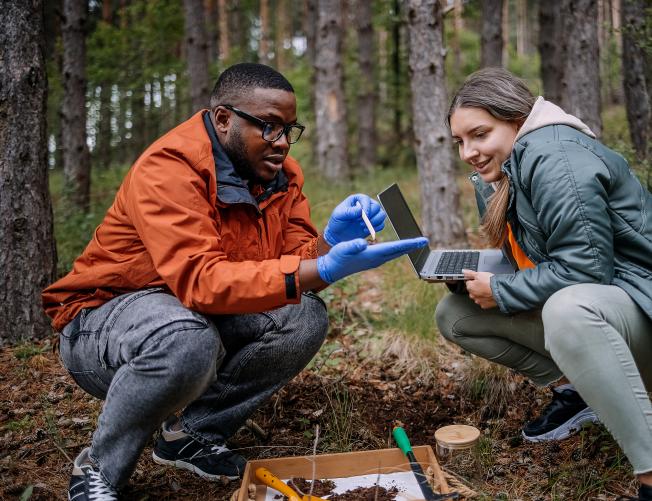biologist explaining project to a science writer outdoors in a forest.