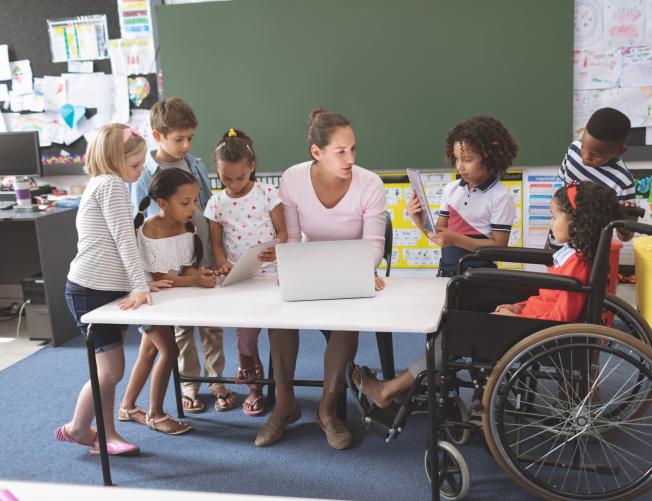 Students using digital tablet while teacher interacting with students in classroom at school