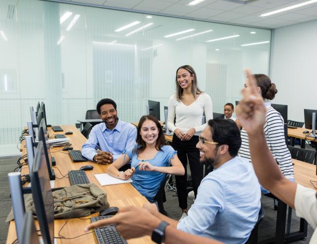Diverse group of students actively participating in a computer lab class, showing engagement and teamwork.