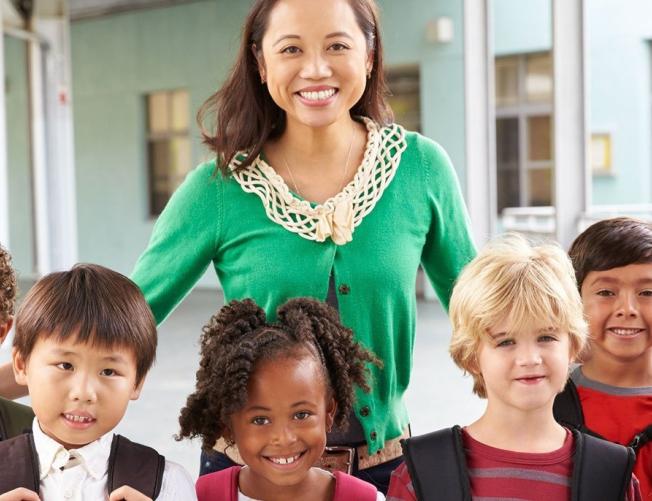teacher and eight small children facing the camera, outside 